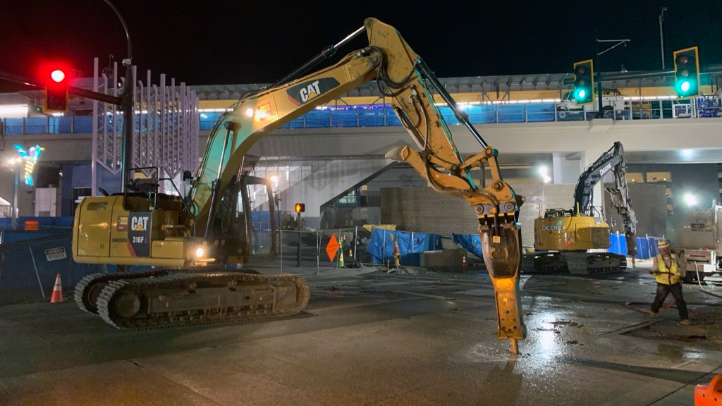 A hydraulic breaker is operated at night to remove a concrete panel in the street.