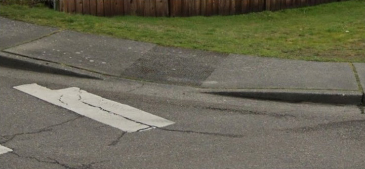 Image showing a part of a cross walk, marked with white paint, leading to a non-compliant curb ramp.