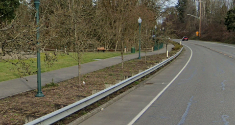 A curved road with a shared-use path running alongside it, separated by a narrow strip of vegetation and a metal guardrail.