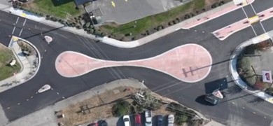 An overhead view of a four-legged roundabout that has one lane for each direction. The roundabout is stretched with the center island in the shape of a peanut. The center island also functions as a mountable truck apron. The footprint of the roundabout intersection matches closely to the signalized intersection it replaced.